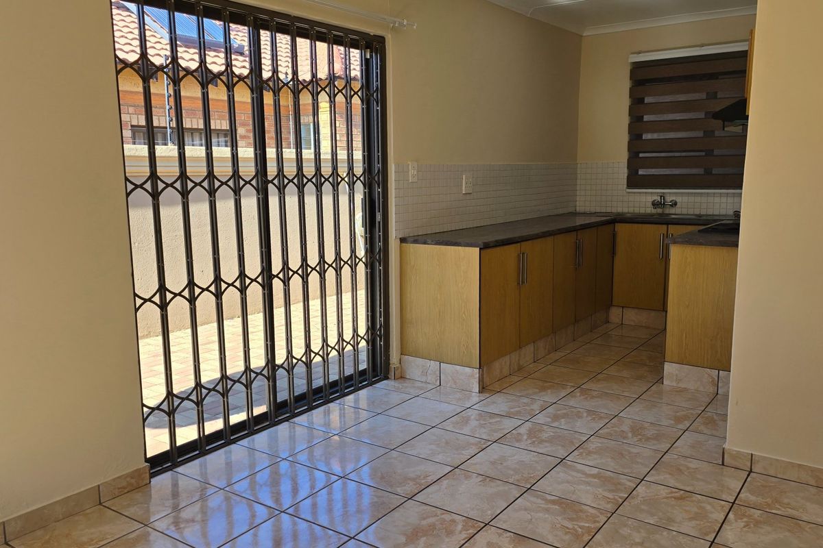 A functional kitchen featuring laminate cabinetry, tiled backsplash, and direct access to the outdoor area through a secure sliding gate.