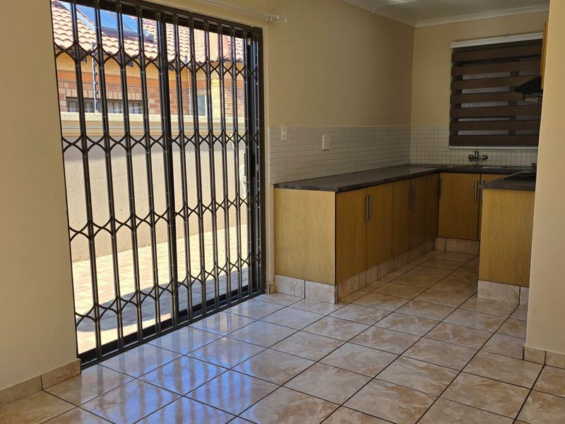A functional kitchen featuring laminate cabinetry, tiled backsplash, and direct access to the outdoor area through a secure sliding gate.