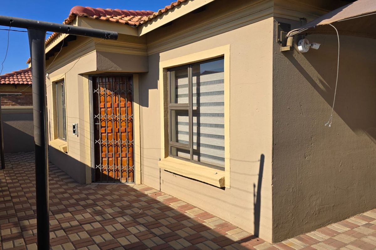 Rear exterior view of the property featuring a paved patio area, security gate, and tiled roof.