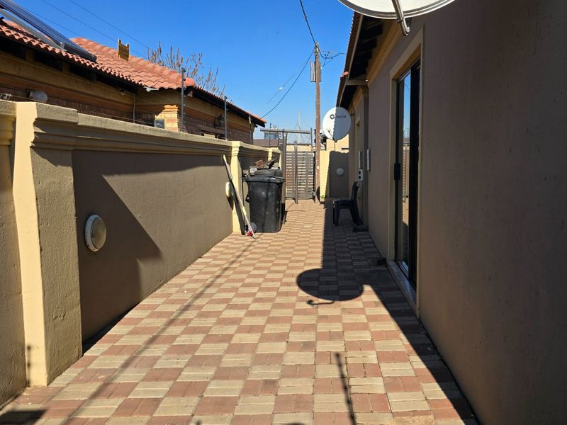A paved side walkway along the exterior of the house, featuring a boundary wall and access via a sliding door.
