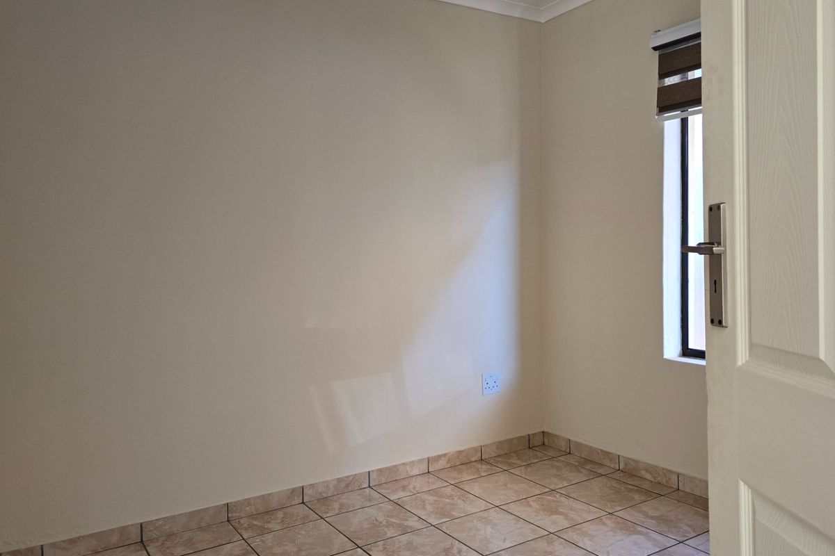 A clean, empty bedroom featuring neutral wall paint, tiled flooring, and a window with a fitted roller blind.