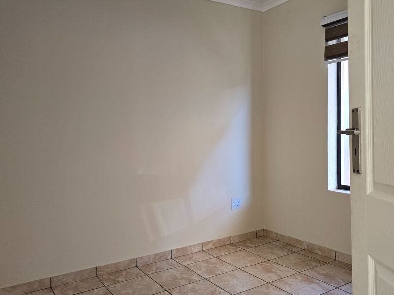 A clean, empty bedroom featuring neutral wall paint, tiled flooring, and a window with a fitted roller blind.