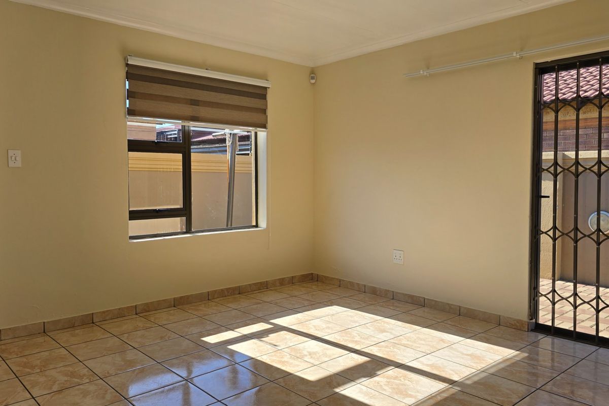 A bright, empty living area featuring tiled flooring, a security gate, and a roller blind, offering a clean and neutral space ready for personalization.