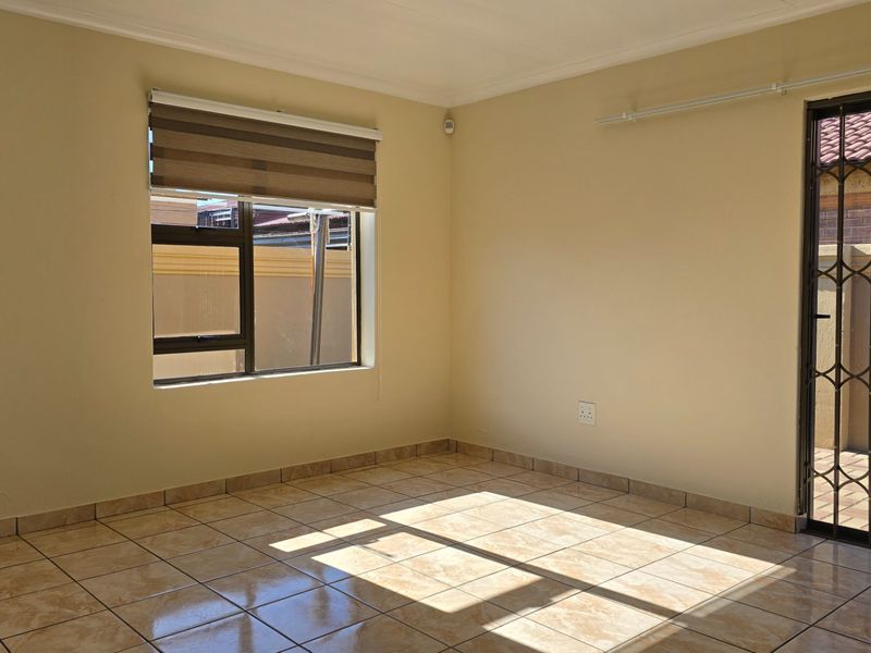 A bright, empty living area featuring tiled flooring, a security gate, and a roller blind, offering a clean and neutral space ready for personalization.