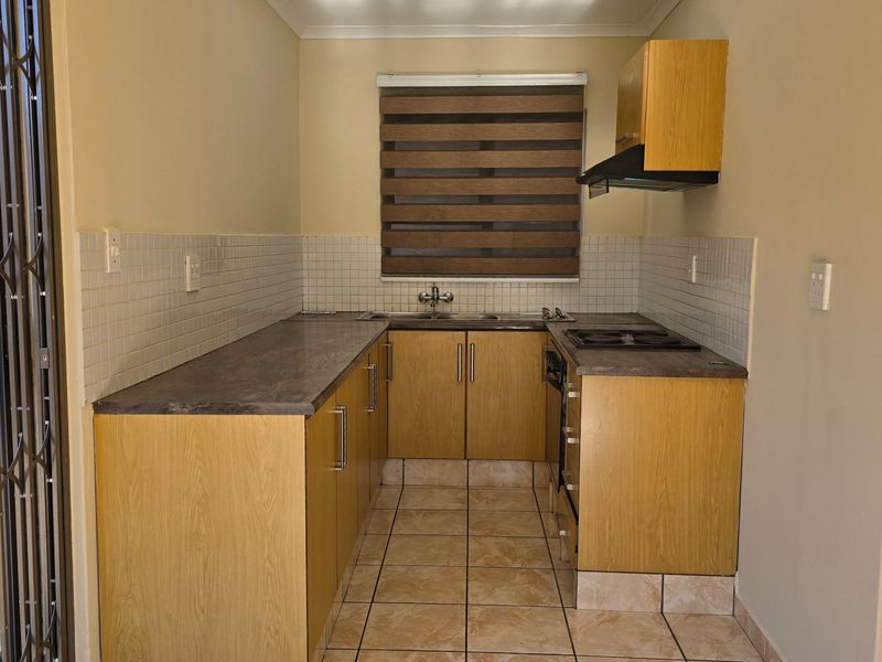 A functional kitchen featuring laminate cabinetry, tiled backsplash, built-in oven and hob, and direct access to the exterior via a security gate.