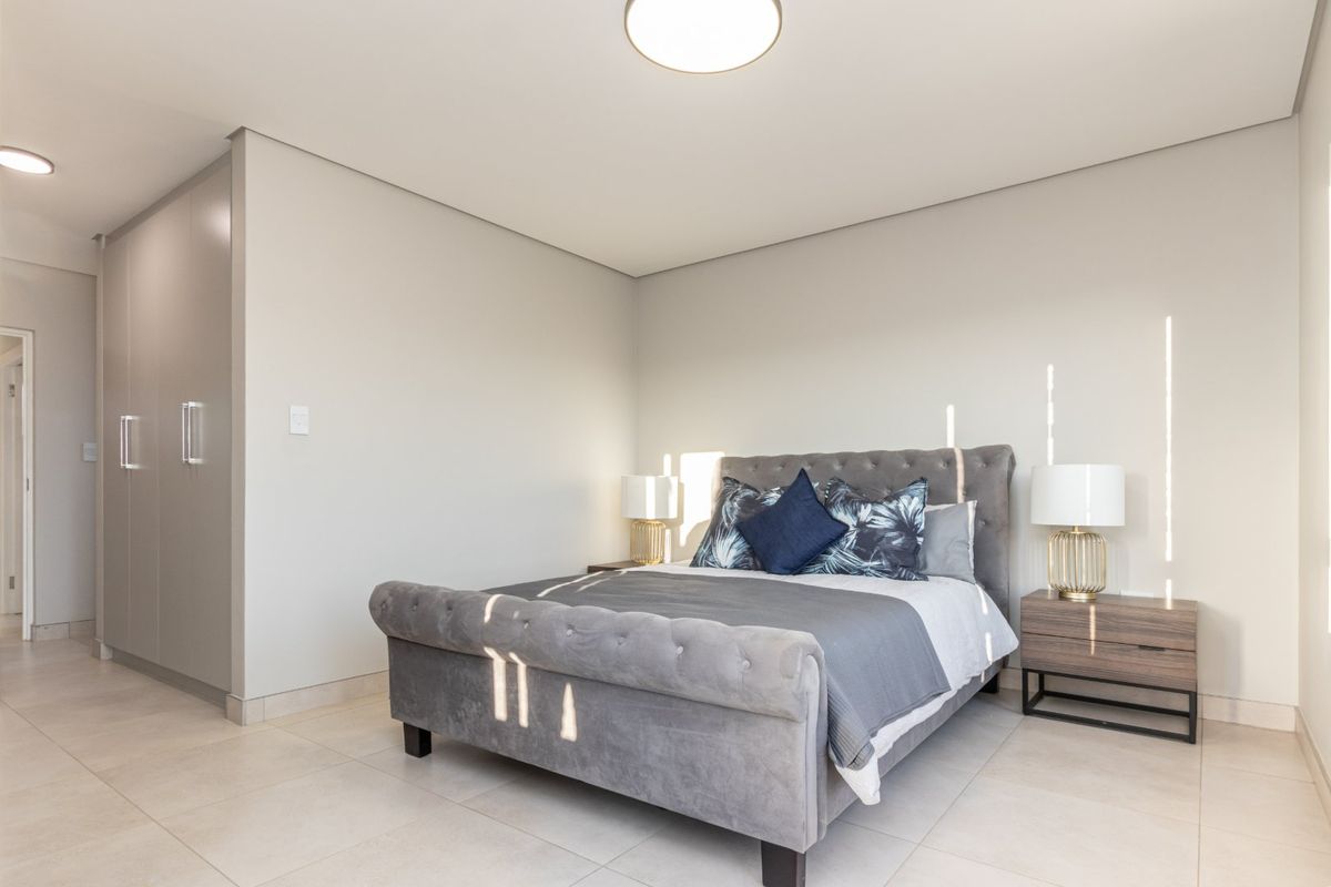 A well-maintained bedroom featuring neutral tiled flooring, built-in cupboards, and modern recessed ceiling lighting, offering a clean and contemporary living space.