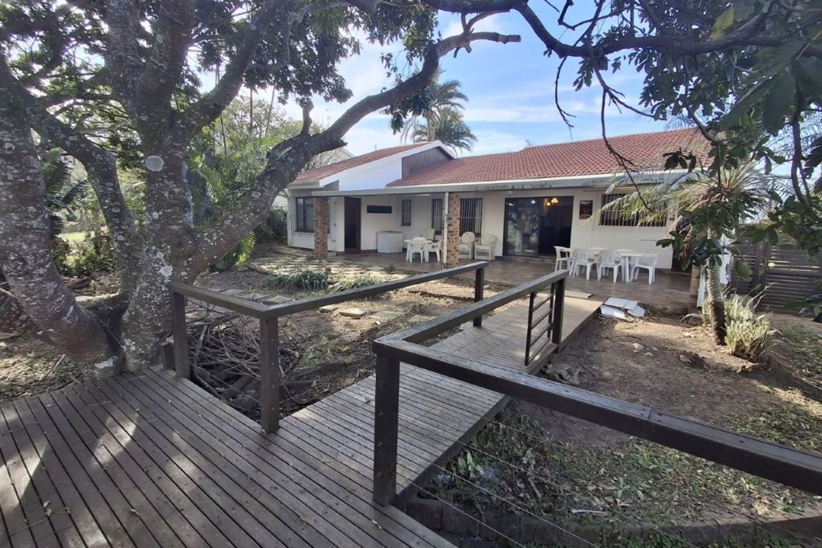 Rear view of the property featuring a timber footbridge leading to a covered patio area with tiled roof and brick support pillars.