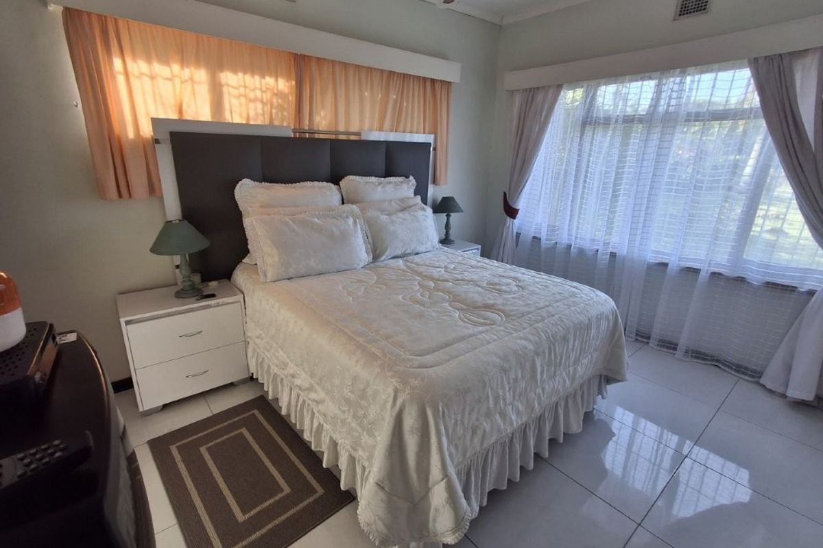 A spacious bedroom featuring large windows, tiled flooring, and a ceiling fan, offering a bright and functional living space.