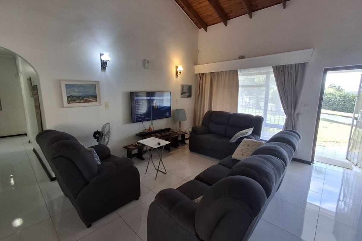 Spacious living room featuring a high vaulted timber ceiling, tiled flooring, and direct access to the outdoor area through a glass door.