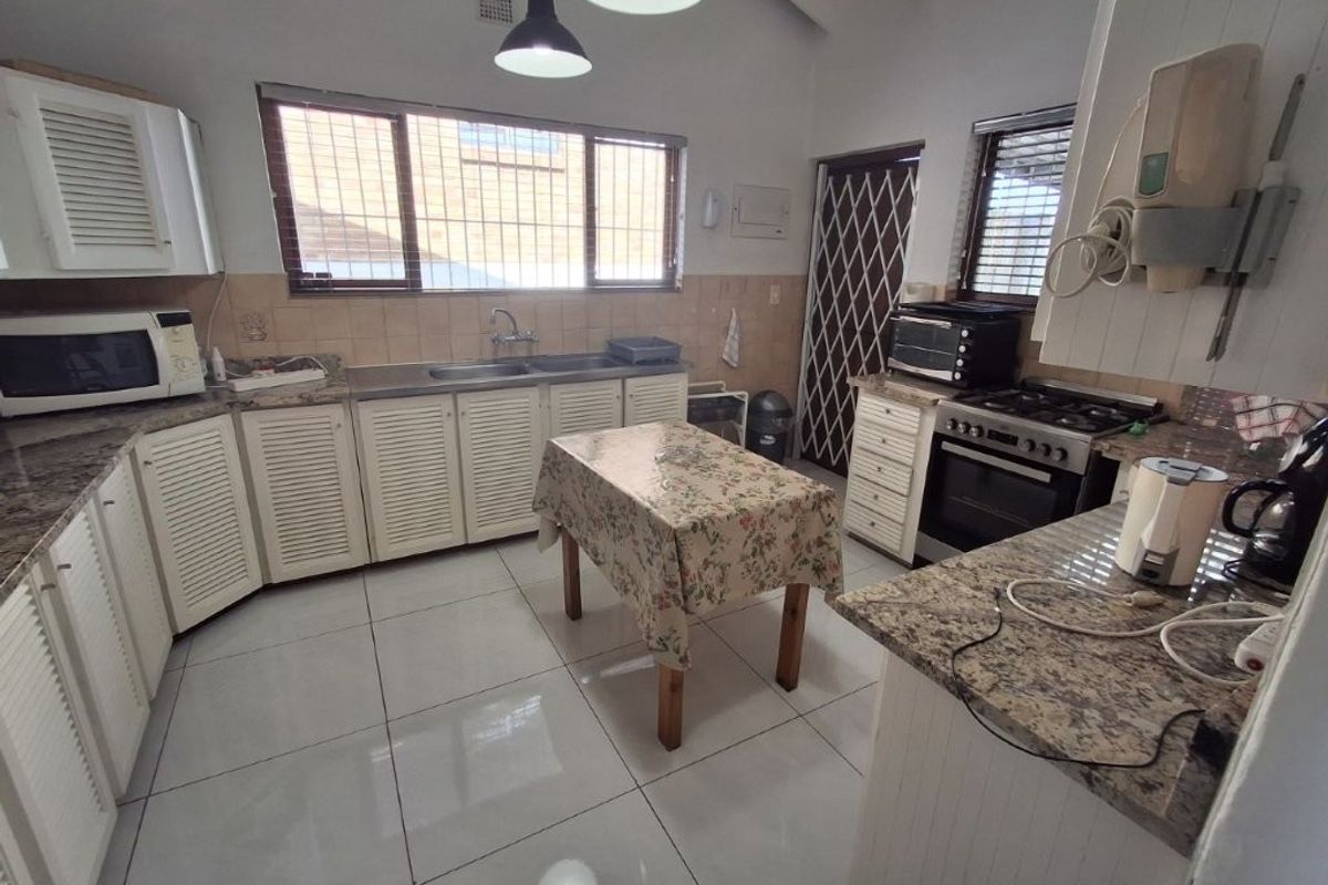 A functional kitchen featuring granite countertops, louvered cabinetry, a double sink, and a freestanding gas stove with tiled flooring throughout.