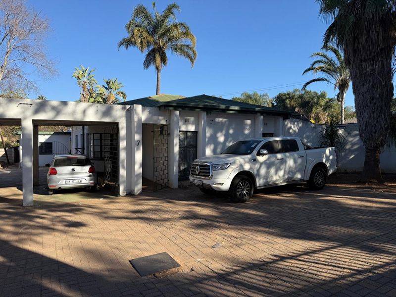 Front exterior view of the property featuring a paved driveway, covered carport, and secure gated entrance.