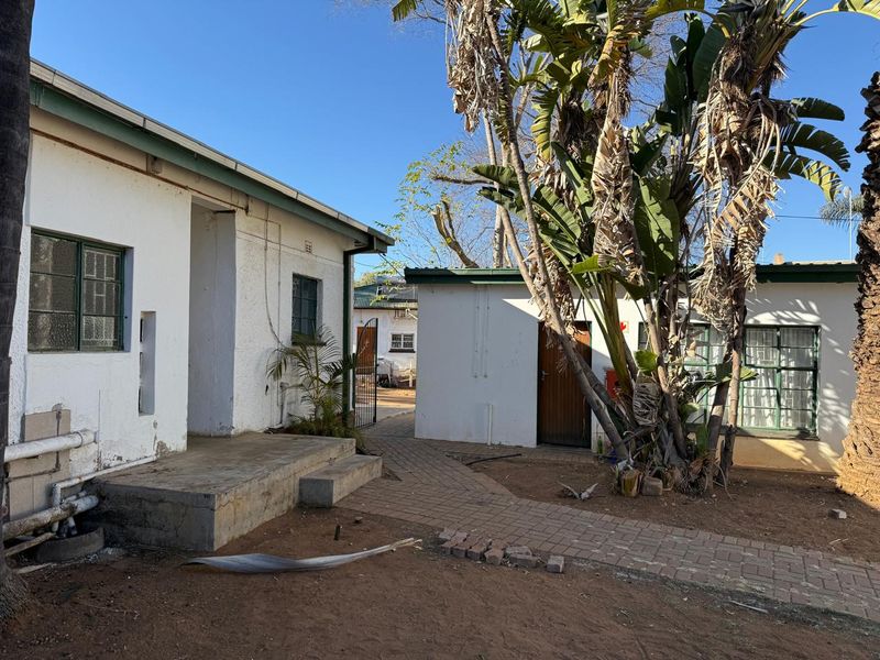 Rear exterior view of the property featuring a paved walkway, concrete porch, and established garden area with mature trees.