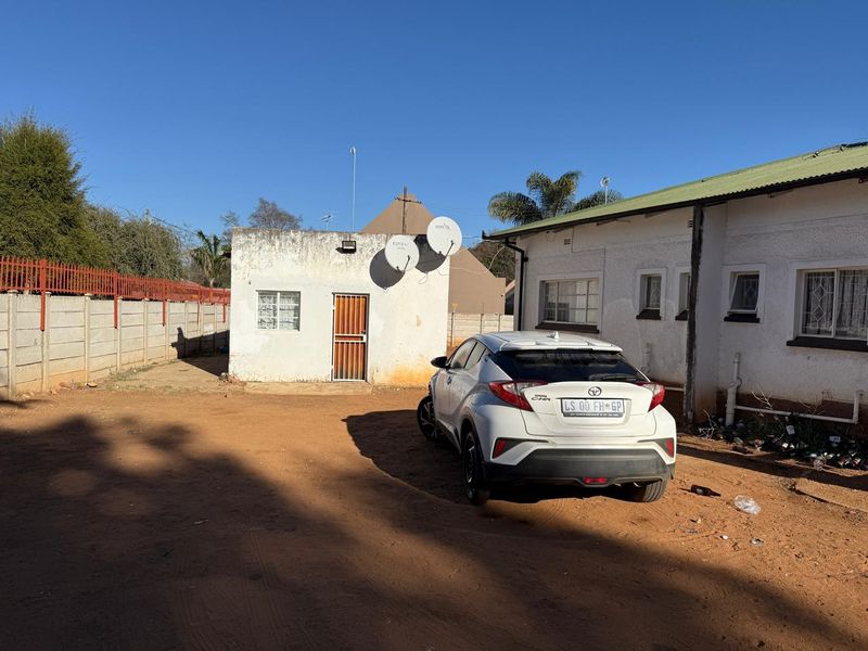 Rear exterior view of the property featuring a detached outbuilding, precast boundary wall, and unpaved yard area.