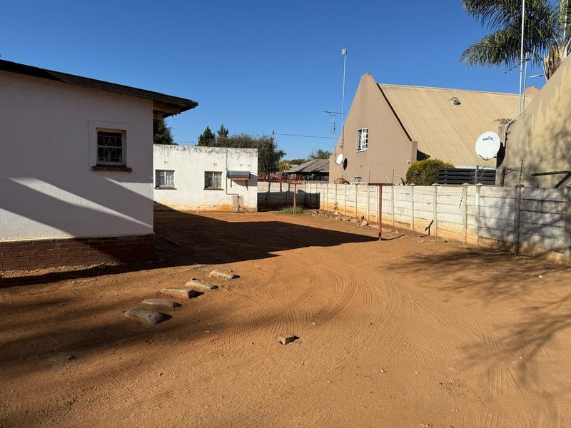 A spacious rear yard area featuring a precast concrete boundary wall, metal washing line, and unpaved ground surface.