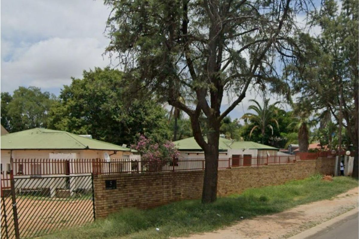 Street view of the property showing the brick boundary wall, metal security fencing, and gated entrance.