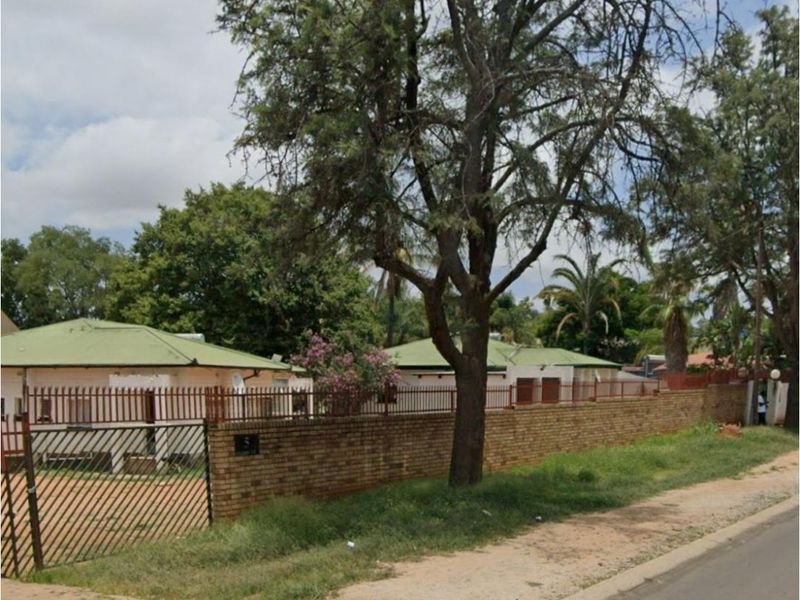 Street view of the property showing the brick boundary wall, metal security fencing, and gated entrance.