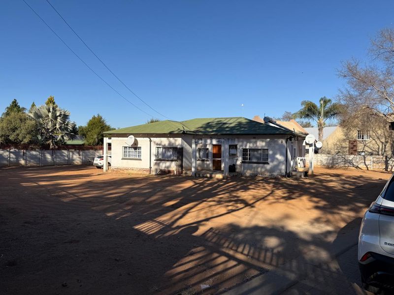 Front view of a single-story residential property featuring a metal roof, solar water heater, and a large unpaved driveway area.
