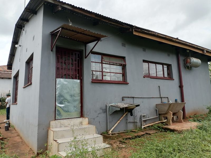 Rear exterior view of the property featuring a corrugated roof, external wash basins, and basic utility infrastructure requiring maintenance and exterior refurbishment.