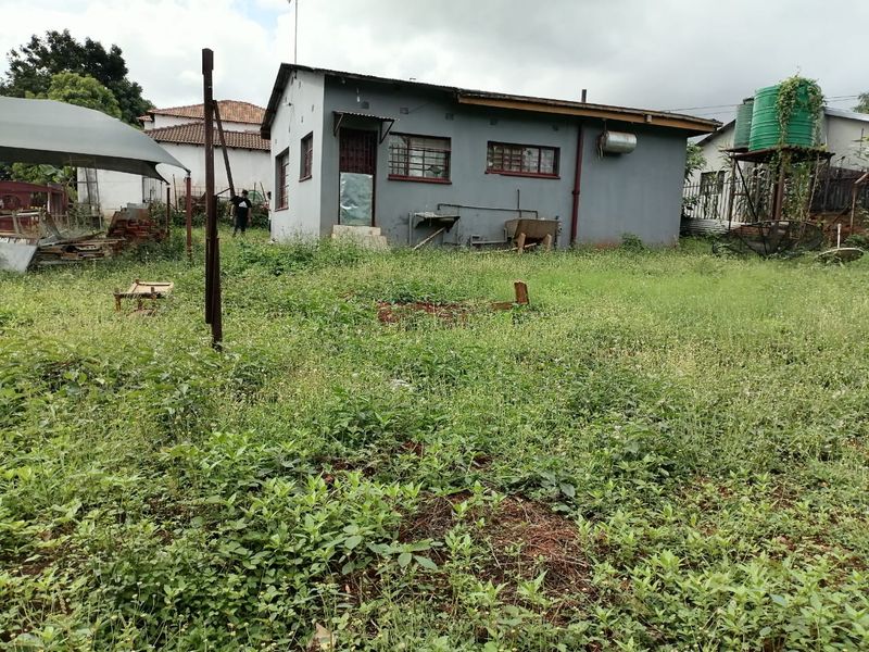 Rear view of a detached house featuring a large overgrown garden area, external water storage tank, and basic masonry construction.