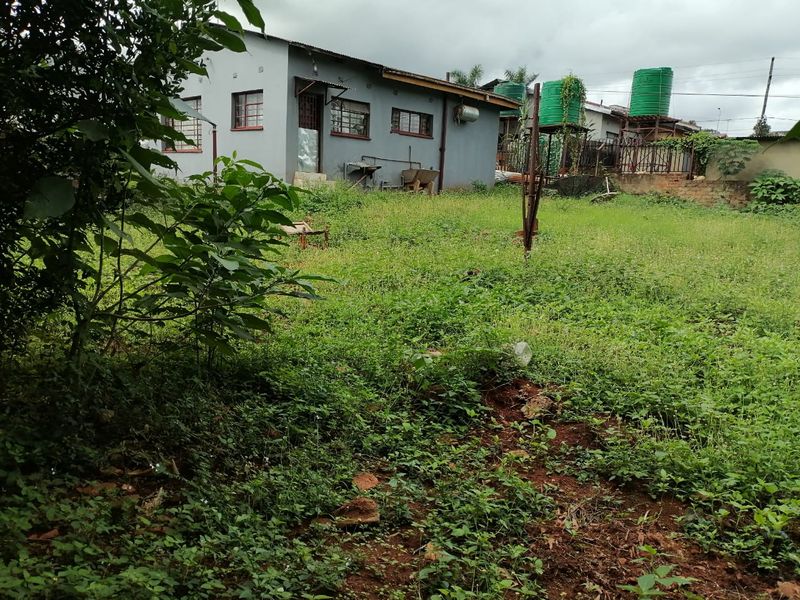 Rear view of the property featuring a large, overgrown garden area, exterior wall with security bars, and elevated water storage tanks.