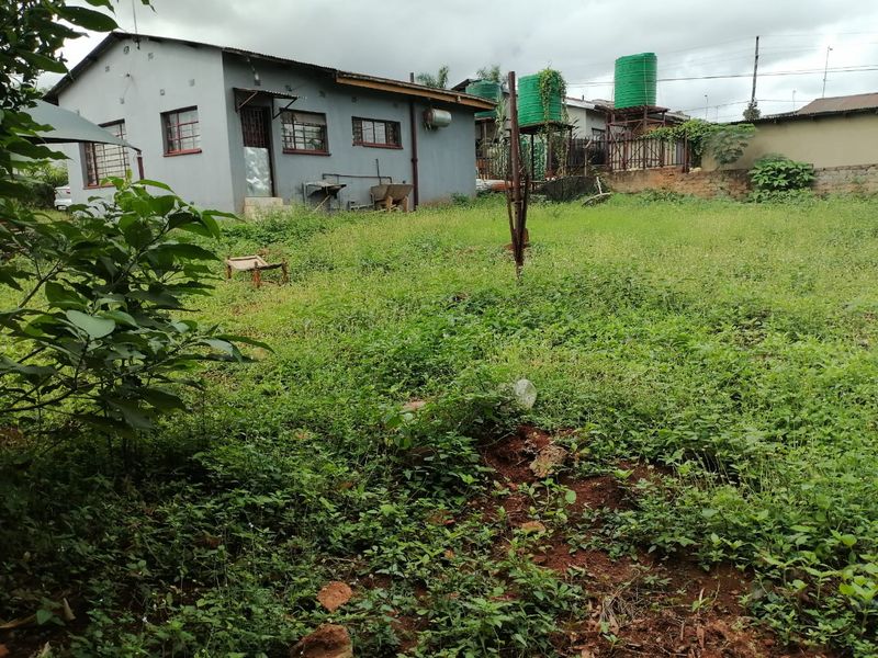 Rear view of the property showing a large, overgrown garden area, exterior wall finishes, and elevated water storage tanks.