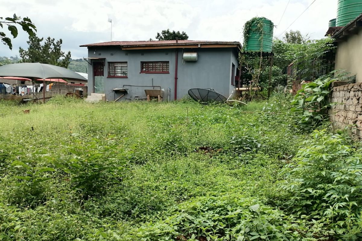 Rear view of the property showing a detached structure with a water tank and an expansive, overgrown garden area.