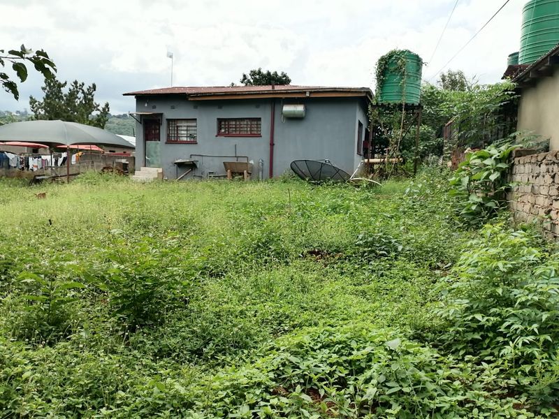 Rear view of the property showing a detached structure with a water tank and an expansive, overgrown garden area.