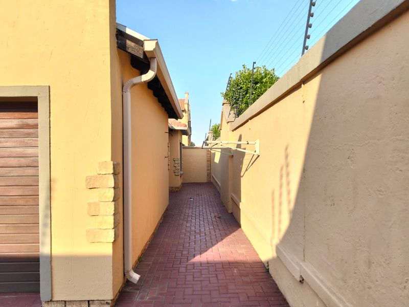 A side passage featuring paved flooring, boundary walls with electric fencing, and a wall-mounted drying rack.