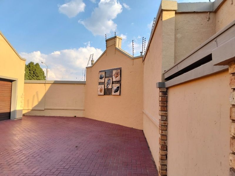 A view of the townhouse exterior featuring a paved driveway, secure boundary walls with electric fencing, and a garage entrance.