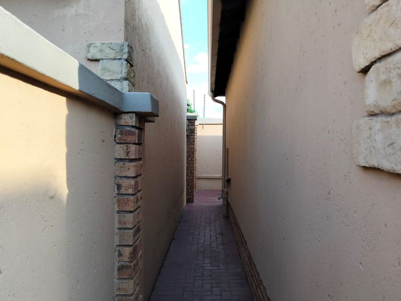 A narrow side passage between two plastered walls featuring paved flooring, brick accents, and integrated security fencing.