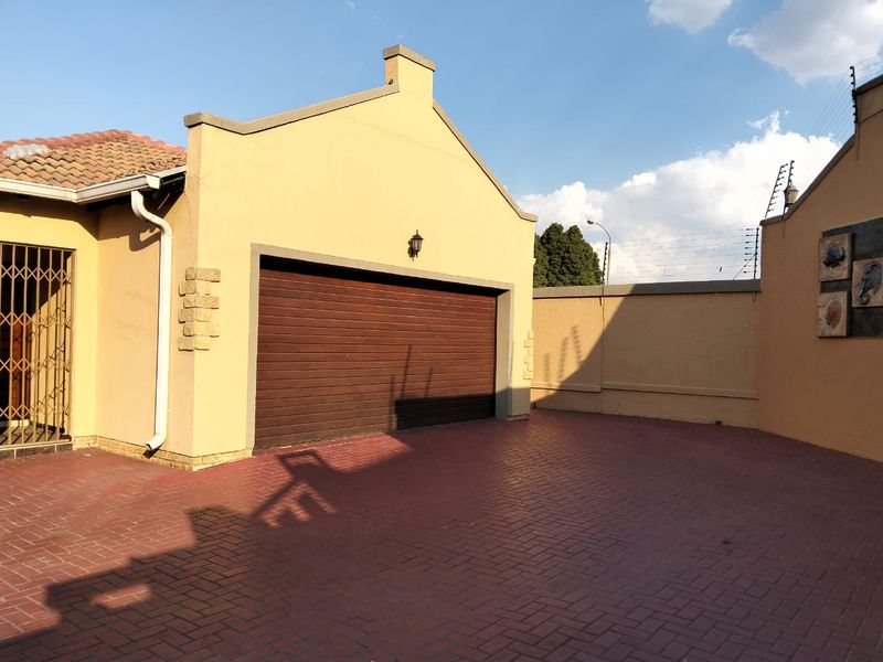 Front exterior view of the townhouse featuring a paved driveway, a secure garage door, and perimeter walling with electric fencing.