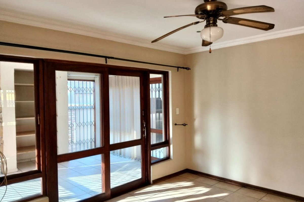 An empty living room featuring tiled flooring, a ceiling fan, and large wooden sliding doors providing access to an outdoor area.