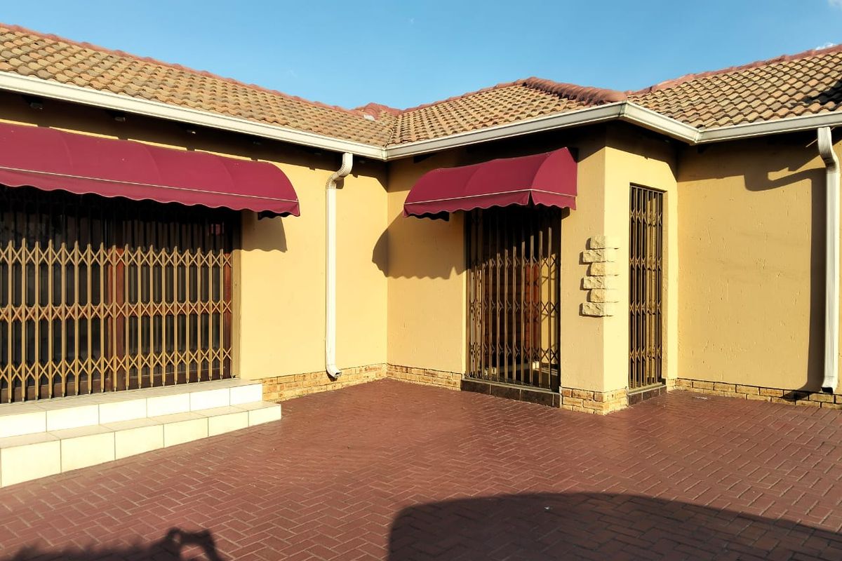 Rear exterior view of the townhouse featuring brick paving, security gates, and protective awnings over the access points.