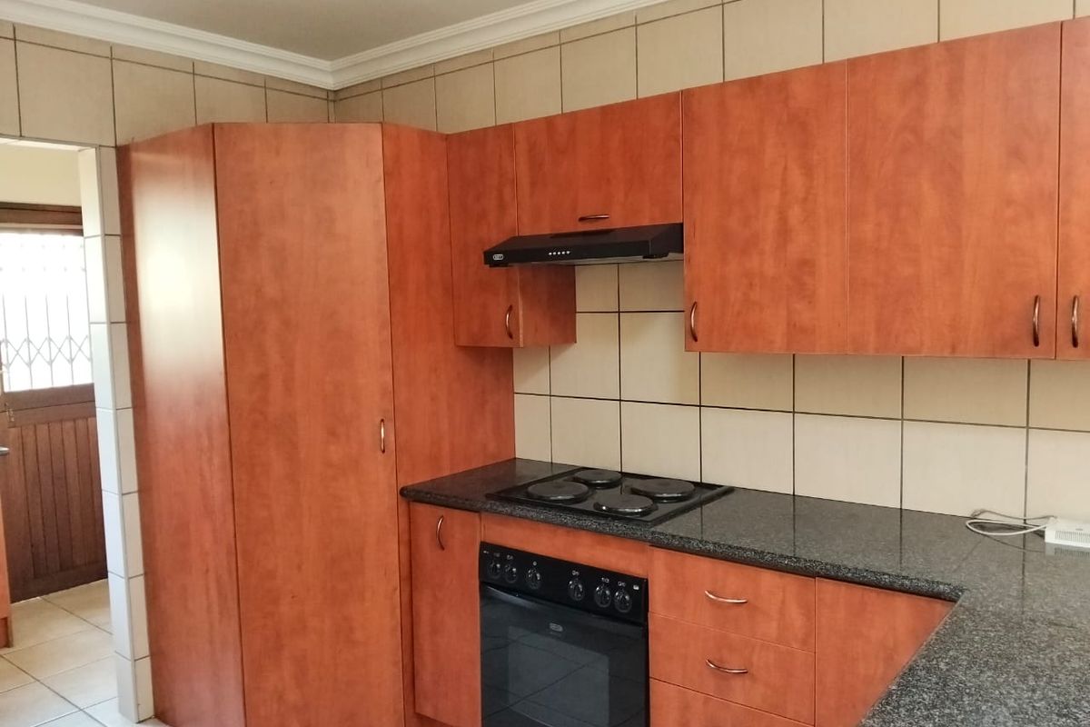 A functional kitchen featuring wood-finish cabinetry, granite countertops, a built-in oven, electric hob, and a tiled backsplash.