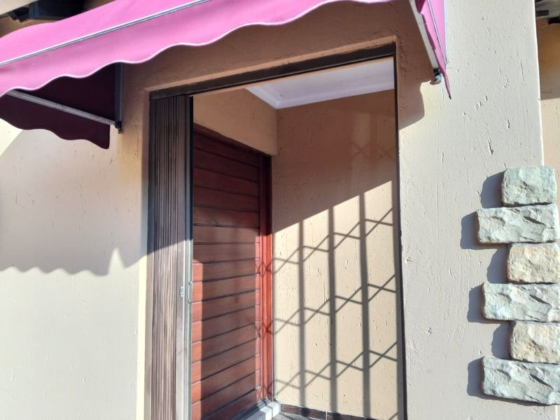 A residential entrance featuring a timber door, security gate, and a retractable awning, accented with decorative stone cladding on the exterior wall.