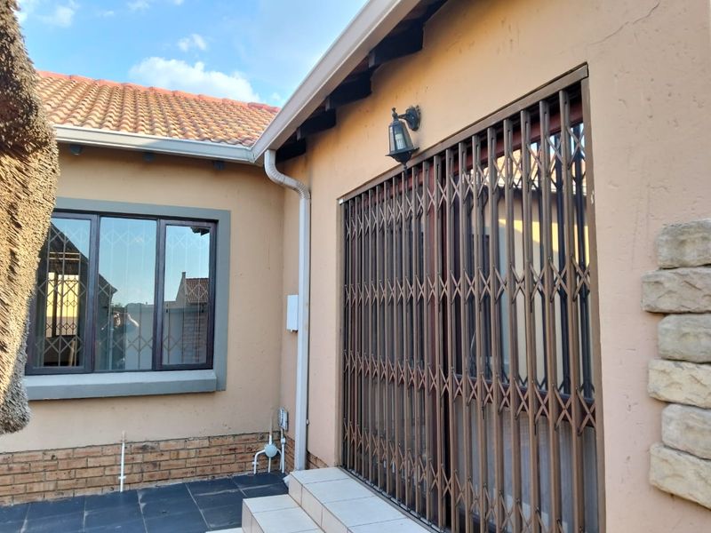 Rear exterior view of the townhouse featuring a tiled patio, sliding door with security gate, and stone cladding accents on the wall.