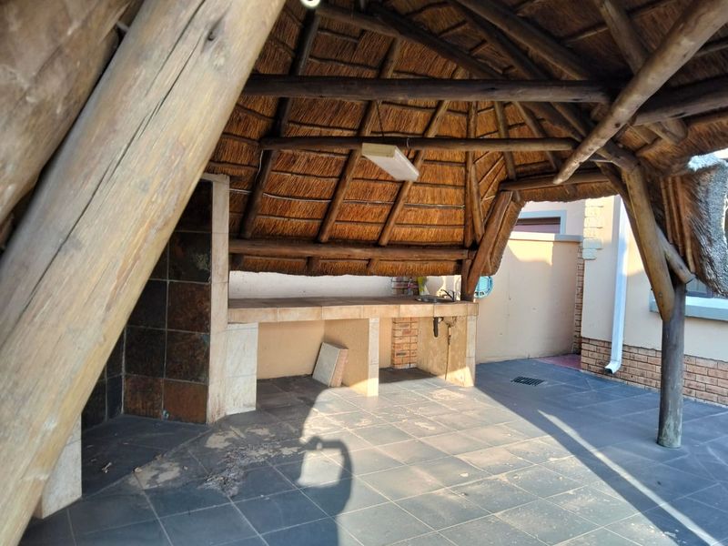 Covered outdoor patio area featuring a traditional thatch roof, timber support structure, and a built-in braai with a tiled prep counter and sink.