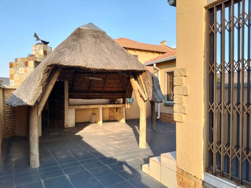 Outdoor patio area featuring a traditional thatched lapa with a built-in braai, tiled flooring, and direct access to the main dwelling.