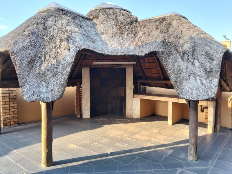 Outdoor entertainment area featuring a traditional thatched roof, built-in braai, and tiled flooring, providing a rustic space for social gatherings.