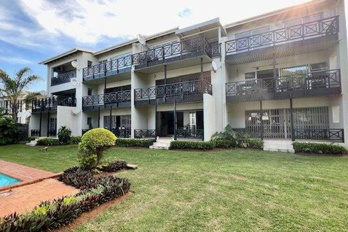 Rear view of the apartment complex featuring multiple levels of balconies, a communal swimming pool, and a well-maintained garden area.