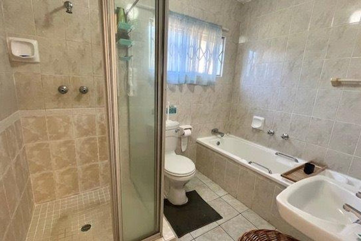 A functional bathroom featuring a separate shower enclosure, bathtub, pedestal basin, and toilet, finished with neutral wall and floor tiling.