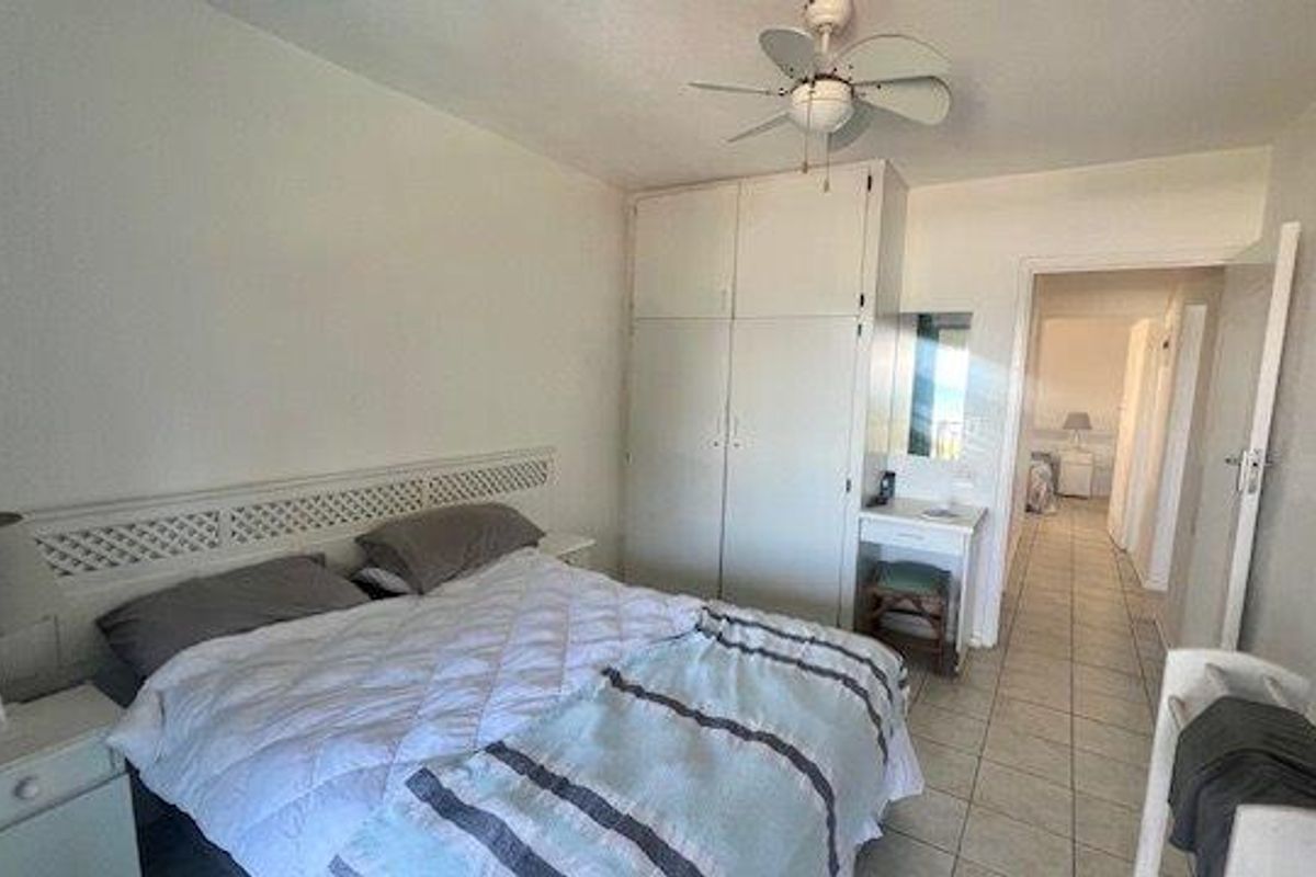 A bedroom featuring built-in wardrobes, a ceiling fan, and tiled flooring, with an adjoining hallway visible through the doorway.