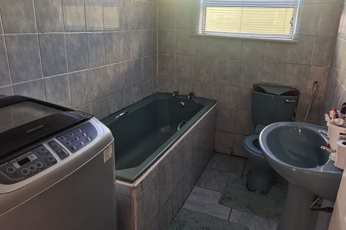A dated bathroom featuring a built-in bathtub, pedestal basin, and toilet with tiled finishes. The space requires maintenance and cosmetic updates.