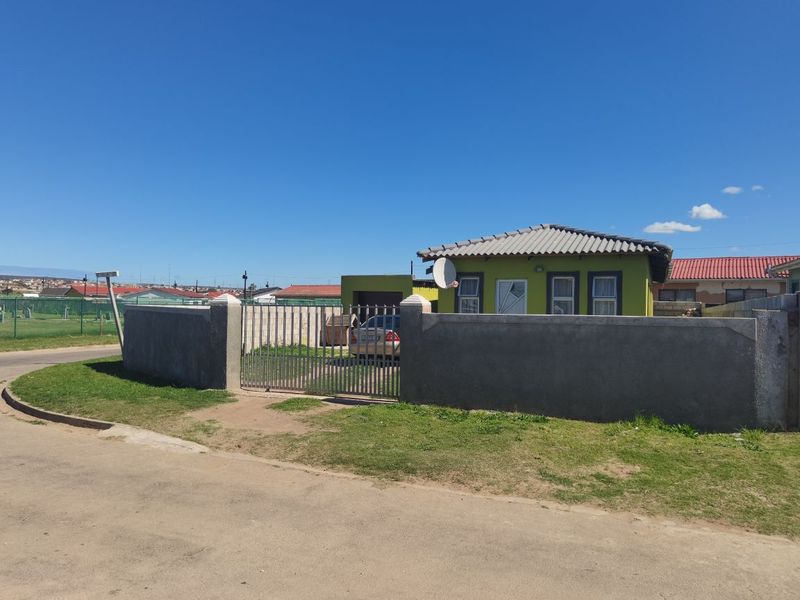 Front view of a single-story house featuring a perimeter wall, metal gate, and tiled roof, situated on a corner plot.