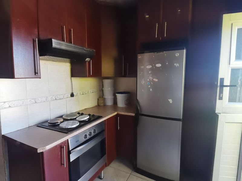A functional kitchen featuring dark wood-finish cabinetry, laminate countertops, a built-in oven, hob, and extractor fan with a tiled backsplash.