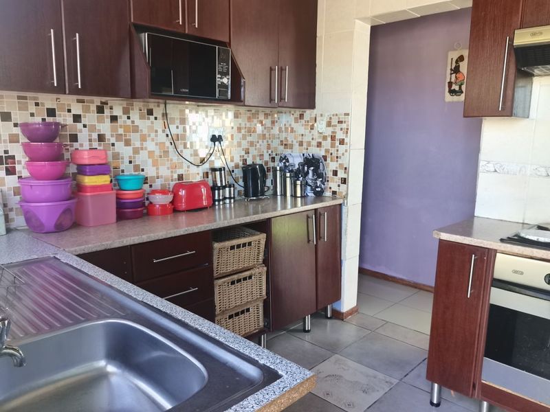 A functional kitchen featuring dark wood-look cabinetry, mosaic tile backsplash, built-in oven, extractor fan, and stainless steel sink with tiled flooring.