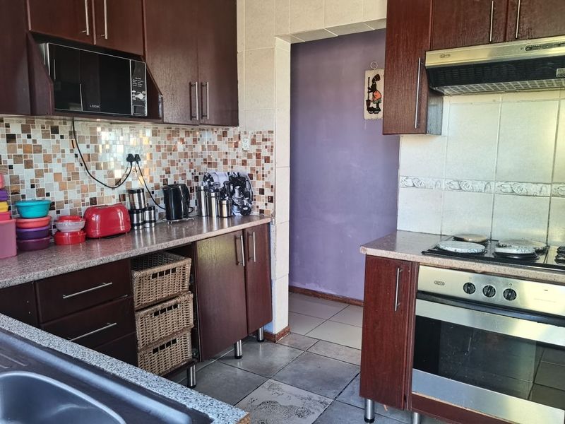 A functional kitchen featuring dark wood cabinetry, mosaic tile backsplash, built-in oven, and hob with ceramic floor tiles.