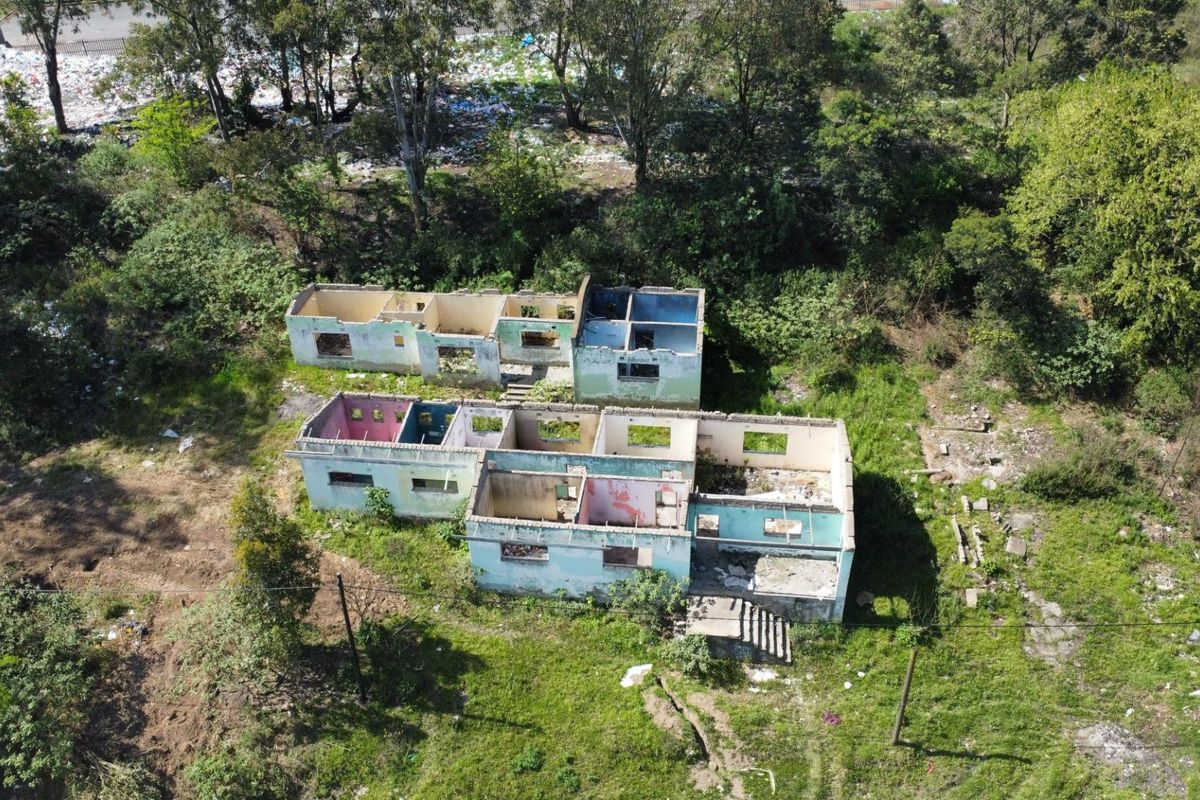 Aerial view of a residential property shell in a state of advanced deterioration, featuring masonry walls on a large overgrown plot.