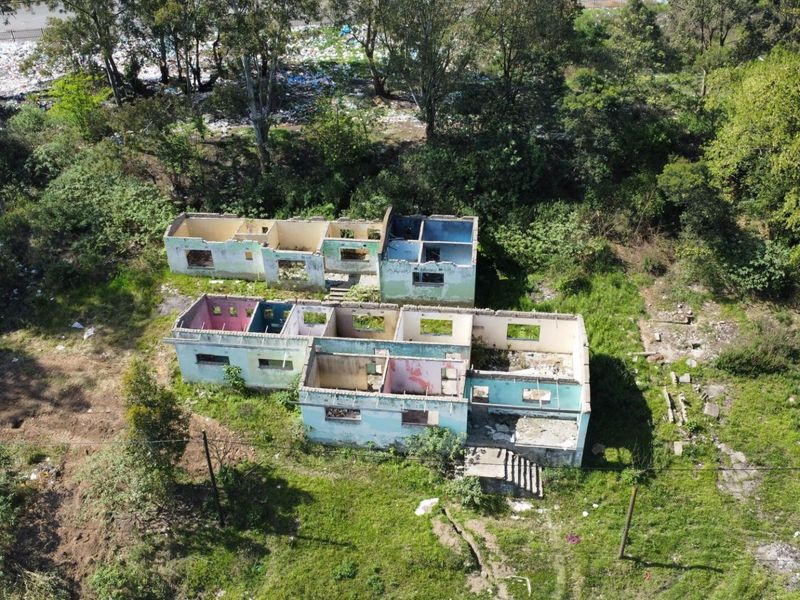 Aerial view of a residential property shell in a state of advanced deterioration, featuring masonry walls on a large overgrown plot.