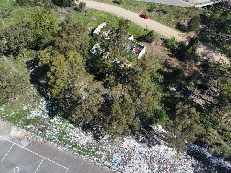 Aerial view of a vacant residential plot featuring mature trees, a dilapidated structure, and significant debris accumulation on the site.